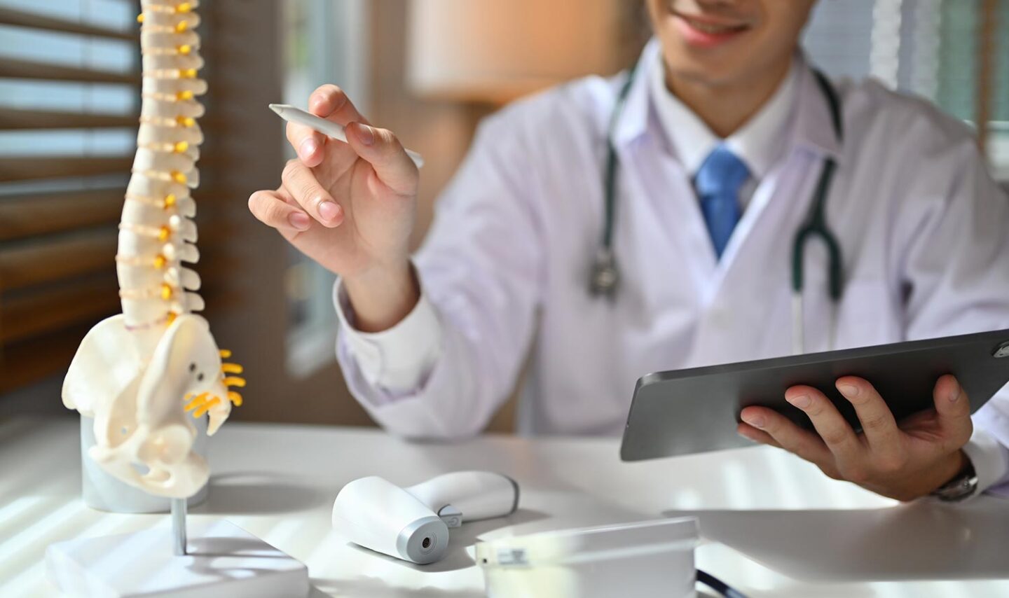 A skilled neurosurgeon studies a replica of a vertebral column meticulously in his clinical workspace.